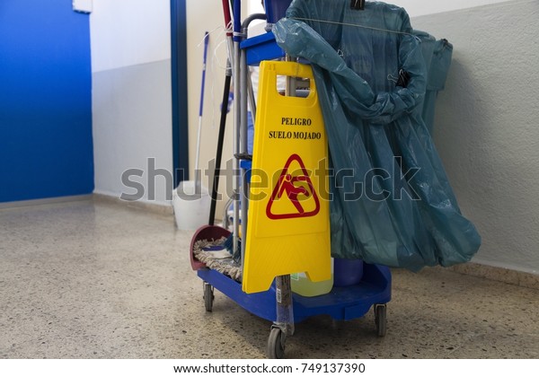 a cleaning trolley with yellow wet floor\
precaution in spanish sign on it and a blue bag on tile floor with\
some cleaning stuff mop and a\
bucket