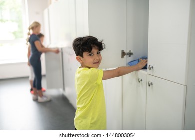 Cleaning Up. Smiling Pupil Standing In Front Of His Locker In Changing Room Putting His Bag There.