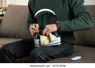 Cleaning Virtual Reality Headset. Person Sitting On Sofa At Home Uses Cloth To Wipe Off Dust From Vr Glasses Optics