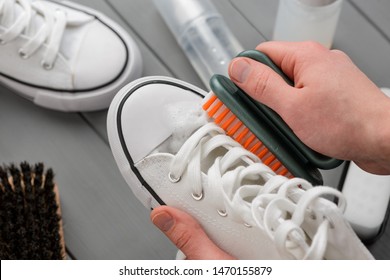 Cleaning White Canvas Sneakers, Closeup Shot. Man Using A Brush And Detergent To Remove The Dirt And Freshen Shoes.