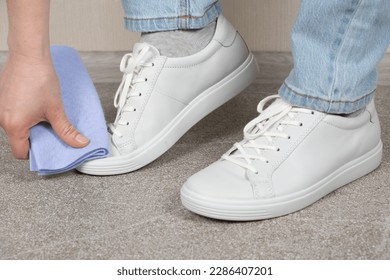 Cleaning white shoes, caring for sneakers. A woman wipes her leather shoes with a wet cloth from dust and dirt