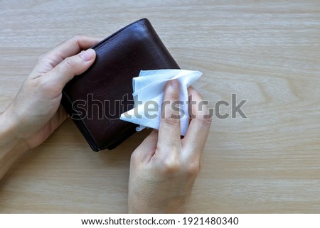 Cleaning and wiping man’s dark brown wallet by alcohol sanitizer clean pad on wooden table background , for disinfect virus bacteria, prevent from epidemic of disease during the corona virus outbreak.
