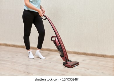 Cleaning Woman In Black Leggins Is Vacuuming With Help Of Upright Vacuum Cleaner With Led Lights On.