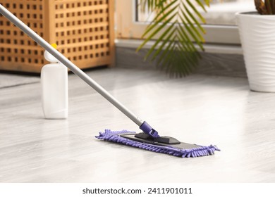 Cleaning of wooden laminate floor with mop and detergent in light room