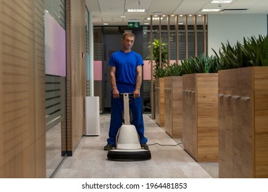 
Cleaning worker in a blue uniform polishing floor in an office