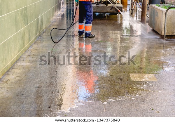 Cleaning worker throwing pressure water to clean\
the sidewalks of a\
city.