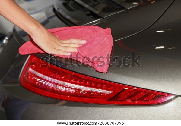 A cleaning worker\'s hand holds a dry\
towel to wipe the dust off the black\
supercar.