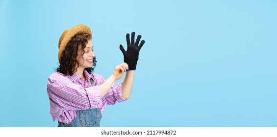 Cleanliness. Flyer With Happy Young Girl, Gardener In Work Uniform And Hat Putting Glove On Isolated On Blue Background. Concept Of Job, Emotions, Agronomy. Funny Meme Emotions. Copy Space For Ad