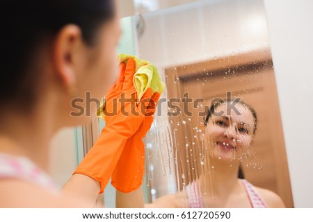 Cleanness in every move. Pretty brunette cleans mirror with help of yellow cloth and special mean of cleaning