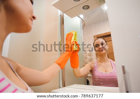 Cleanness in every move. Pretty brunette cleans mirror with help of yellow cloth and special mean of cleaning
