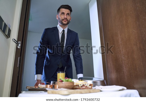 Clean-shaven\
professional staff member is bringing a cart with the ordered\
selection of food into a guest\
room