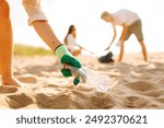 Cleanup garbage on the ocean coast. Volunteers with polyethielene bag picking up a plastic bottle on the beach. The concept of conservation of ecology. Earth day.