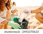 Cleanup garbage on the ocean coast. Volunteers with polyethielene bag picking up a plastic bottle on the beach. The concept of conservation of ecology. Earth day.