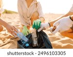 Cleanup garbage on the ocean coast. Volunteers with polyethielene bag picking up a plastic bottle on the beach. The concept of conservation of ecology. Earth day.