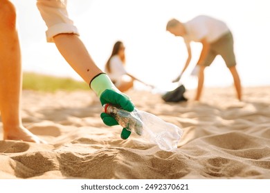 Cleanup garbage on the ocean coast. Volunteers with polyethielene bag picking up a plastic bottle on the beach. The concept of conservation of ecology. Earth day. - Powered by Shutterstock