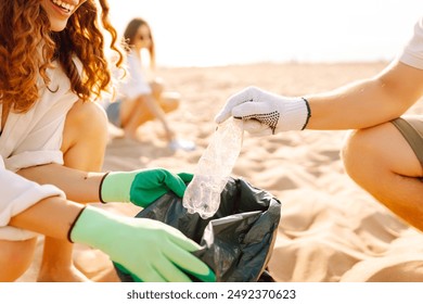 Cleanup garbage on the ocean coast. Volunteers with polyethielene bag picking up a plastic bottle on the beach. The concept of conservation of ecology. Earth day. - Powered by Shutterstock