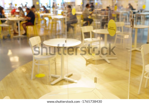 Clear acrylic or plastic divider, barrier or partition\
on empty table in food court or restaurant as part of safety\
protection for customers. New normal, social distancing during\
Covid-19 pandemic 