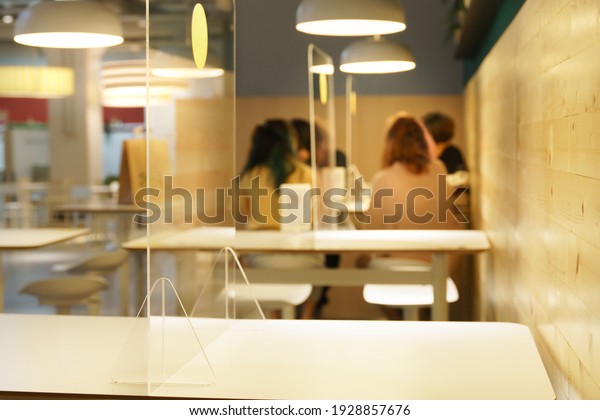 Clear acrylic or plastic divider, barrier or partition\
on empty table in food court as part of safety protection for\
customers in background. New normal, social distancing during\
Covid-19 pandemic 