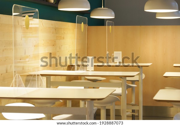 Clear acrylic or plastic divider, barrier or partition\
on empty table in food court or restaurant as part of safety\
protection for customers. New normal, social distancing during\
Covid-19 pandemic 