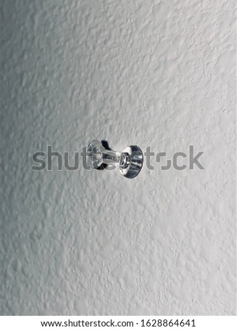 Clear average sized thumb tack pushed into a white textured wall.