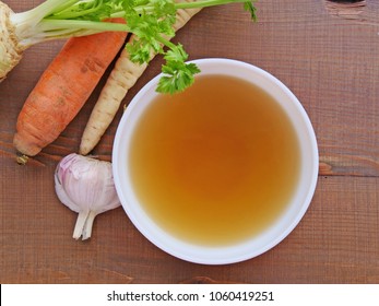 Clear beef broth, bone broth, bouillon in white bowl and vegetables on wooden table top view