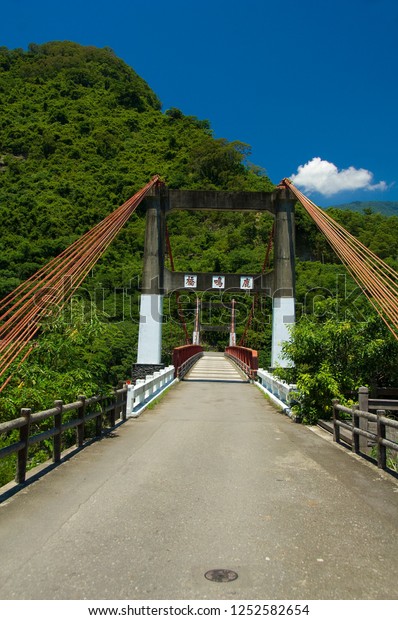 A clear blue sky, a bridge leading to the brown\
steel ropes of the Green Mountains. White traditional Chinese on\
the bridge: Luming Bridge.