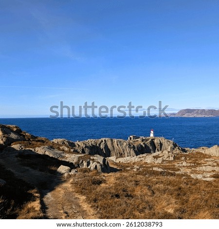  A clear blue sky frames the rugged trail leading to the red and white Varnes lighthouse.
Set against the Atlantic coast, this view captures the Norwegian shoreline's raw beauty