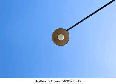 Clear blue sky frames a simple circular object. Black wire extends diagonally across the frame. Brown disc hangs suspended, appearing isolated and still