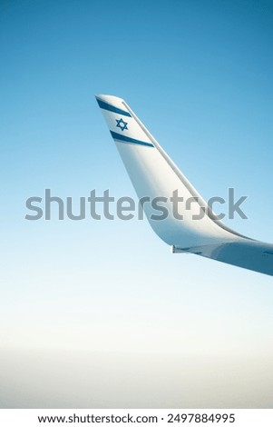 A clear blue sky frames the wing of an El Al airplane, proudly displaying the Israeli flag. This serene in-flight moment captures the essence of travel and aviation, showcasing El Al's commitment 