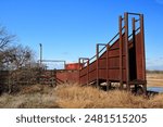 A clear blue sky, rusty, rugged cattle chute and corral lie abandoned on a quiet roadside in the far west plains of Texas