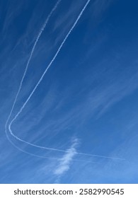 A clear blue sky with soft clouds and distinct plane tracks streaking across, creating a minimalist yet dynamic composition