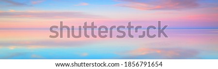 Clear blue sunset sky with glowing pink clouds above the sea. Symmetry reflections on the water, natural mirror. Breathtaking panoramic scenery. Idyllic landscape. Climate change, beauty in nature