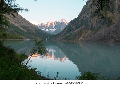 Clear blue water in a mountain lake. Snowy peaks and mountain slopes are reflected in the lake at sunset.Summer evening - Powered by Shutterstock