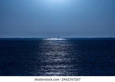 Clear, bluish night sky illuminated by moonlight with its rays of light beautifully reflected in the water of the Mediterranean Sea and a backlit fishing boat silhouette on the horizon line. - Powered by Shutterstock