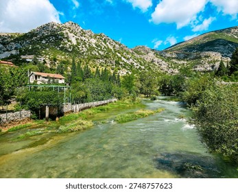 Clear Buna river flowing through green valley near Blagaj village, Bosnia and Herzegovina with mountains, trees and traditional countryside scenery.