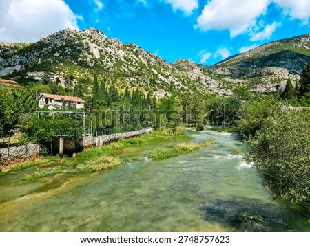 Clear Buna river flowing through green valley near Blagaj village, Bosnia and Herzegovina with mountains, trees and traditional countryside scenery.