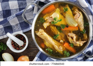 Clear Chicken Broth With Pieces Of Free Range Farm Organic Rooster Meat On Bone In A Metal Casserole With Kitchen Towel And Ingredients On Wooden Table, View From Above, Close-up