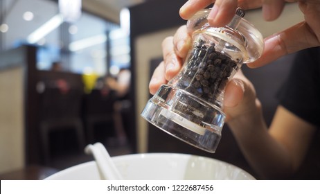 Clear Color Glass And Thailand Black Pepper Mill Or Grinder In Hands That Twisting The Bottle And Pouring Or Adding Small Pieces Of Spices To Plate Or Bowl For A Better Taste In The Meal.