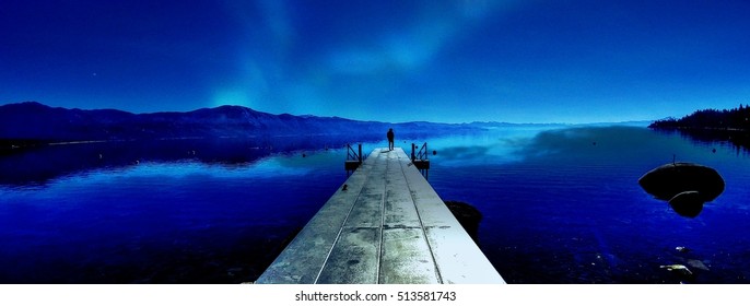 Clear, crisp, bold water and night northern light sky panoramic landscape image of long pier with silhouette of a person at the end under northern lights. - Powered by Shutterstock