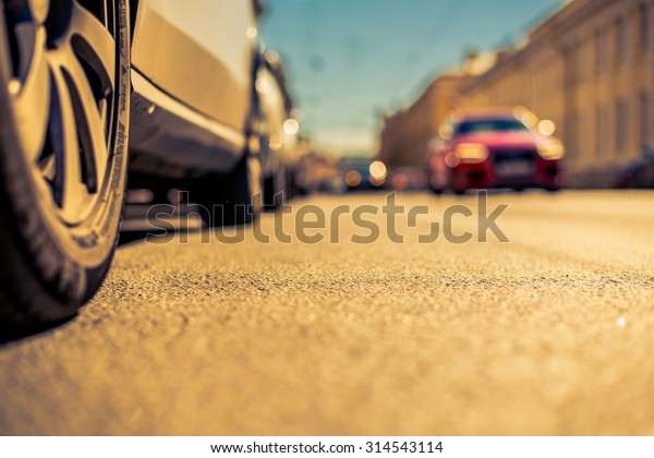 Clear day in the big city, a city\
street with moving cars on it. View from the road level from the\
wheel of the car, image in the yellow-blue\
toning