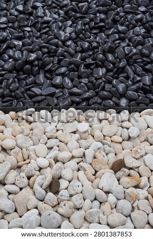 A clear division separates a large collection of polished black pebbles from a mound of smooth, light-colored river rocks, offering a study in texture and color contrast