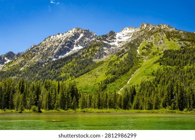 Clear emerald green waters of String Lake stretch toward forested slopes and snowcapped Teton peaks