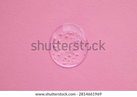 Clear gel droplet with tiny bubbles on soft pink background evokes skincare, beauty and freshness.