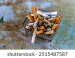 Clear glass ash tray overflowing with cigarette buds and ash.