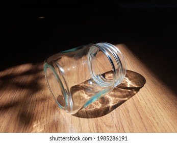 A Clear Glass Bottle Lay Down On The Brown Wood Floor In The Sunlight From The Window.