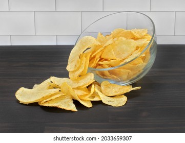 A Clear Glass Bowl Of Potato Chips Tipped And Spilling Onto A Tabletop.