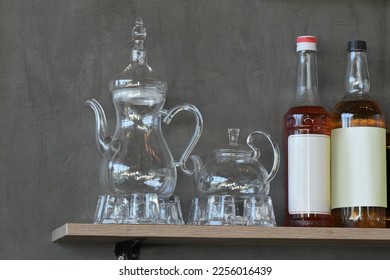 Clear glass jug or kettle and syrup bottles on wooden shelves attached to stucco wall. - Shutterstock ID 2256016439