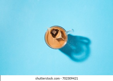 Clear Glass Mug With Coffee, Creamer And Sugar Cube In Top Down View On A Blue Background