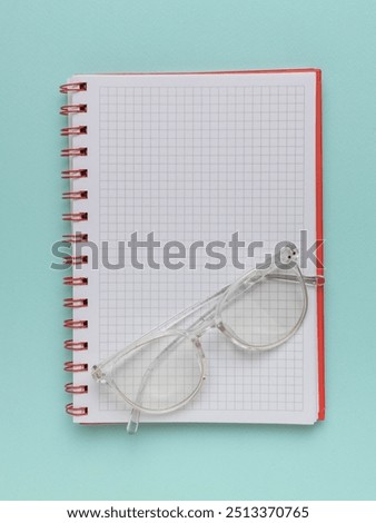 Clear Glasses on a Grid-Patterned Notebook Against a Mint Green Background