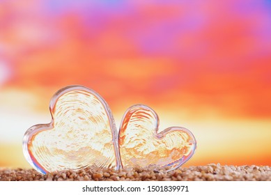 Clear Heart Sea Glass  On  Beach Sand   With Bright Sunrise Or Sunset Background